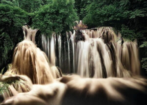 Waterfall Una River – Poster – Fotografi. Vattenfallet breder ut sig över klipporna och omges av frodig grönska.